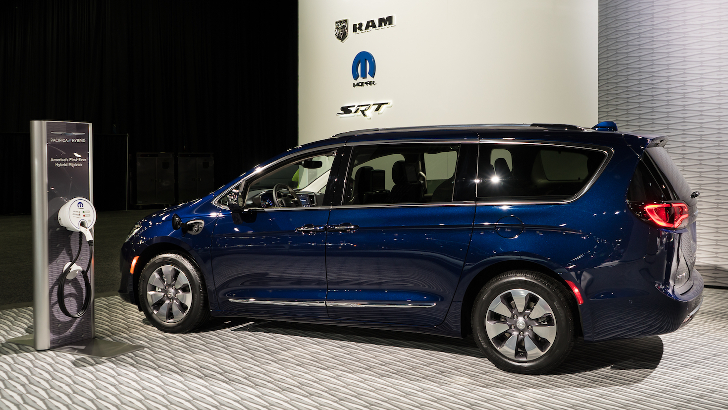 A navy blue Chrysler Pacifica hybrid minivan next to a vehicle charger