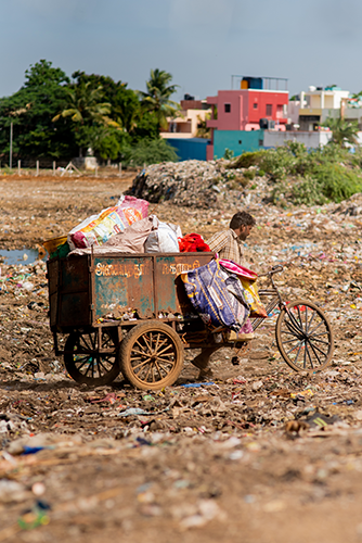 Indian waste picker on a bike that has cart on back filled with waste